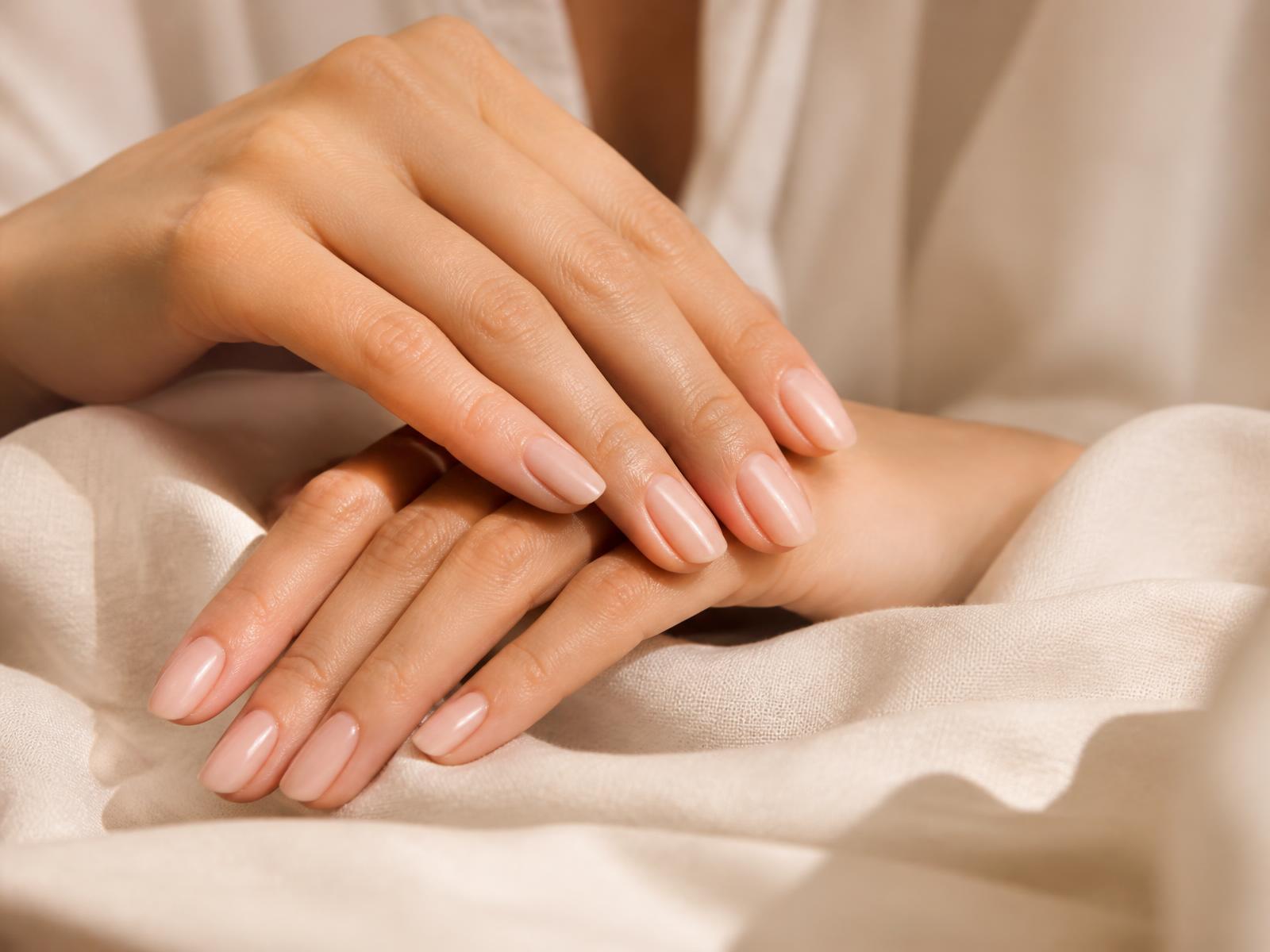 Verzorgde nagels met natuurlijke nude manicure op zachte crème stof